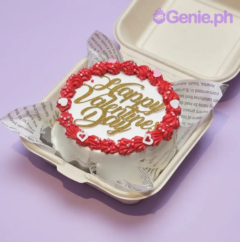 A white Bento cake with red icing rosettes, pink and white heart accents, and a gold glitter 'Happy Valentine's Day' topper. A white Bento cake with red icing rosettes, pink and white heart accents, and a gold glitter 'Happy Valentine's Day' topper.
