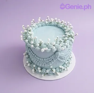 A light blue 1-Tier cake themed around vintage style, featuring intricate piped icing swags and white lily of the valley floral accents. A light blue 1-Tier cake themed around vintage style, featuring intricate piped icing swags and white lily of the valley floral accents.