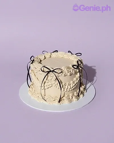 A white 1-tier cake with a vintage minimalist theme, featuring black ribbon bows and intricate cream piping. A white 1-tier cake with a vintage minimalist theme, featuring black ribbon bows and intricate cream piping.