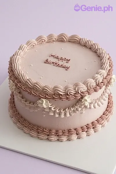 A light pink 1-tier vintage cake with piped borders, swags, white rosettes, and 'Happy Birthday' text.
