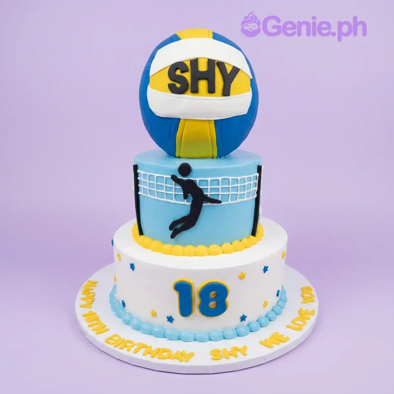 A blue, yellow, and white two-tier volleyball cake, with a volleyball, player silhouette, and number 18. A blue, yellow, and white two-tier volleyball cake, with a volleyball, player silhouette, and number 18.