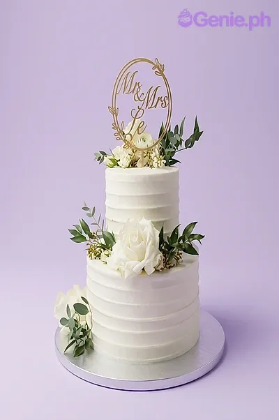 White 2-tier wedding cake with textured soft icing, a Mr & Mrs circular topper, and fresh white roses with greenery. White 2-tier wedding cake with textured soft icing, a Mr & Mrs circular topper, and fresh white roses with greenery.