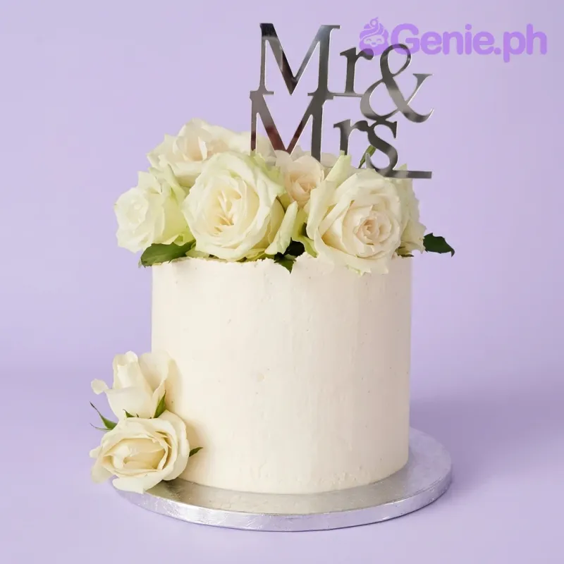 A white single-tier cake themed around a wedding, featuring a silver Mr & Mrs cardstock topper and fresh white roses. A white single-tier cake themed around a wedding, featuring a silver Mr & Mrs cardstock topper and fresh white roses.