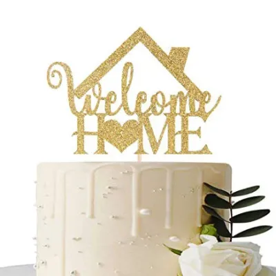 A white 1-tier cake themed around Welcome Home, featuring a gold glitter house topper, white chocolate drip, silver dragees, and a white rose with green leaves. A white 1-tier cake themed around Welcome Home, featuring a gold glitter house topper, white chocolate drip, silver dragees, and a white rose with green leaves.