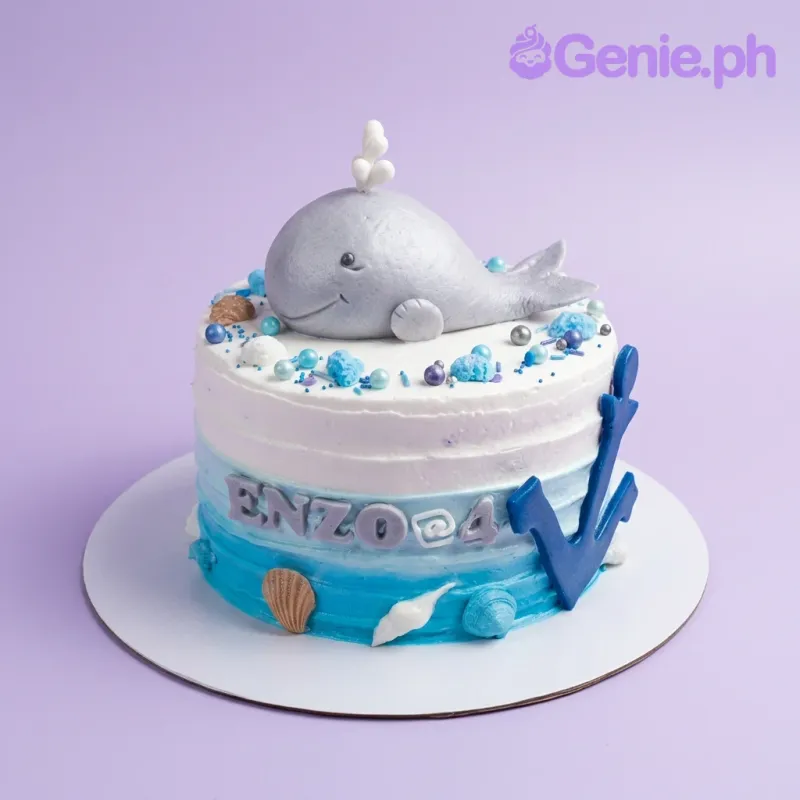 A blue and white ombre 1-tier cake themed Whale Ocean, featuring a grey whale topper, blue anchor, and orange sea shells. A blue and white ombre 1-tier cake themed Whale Ocean, featuring a grey whale topper, blue anchor, and orange sea shells.