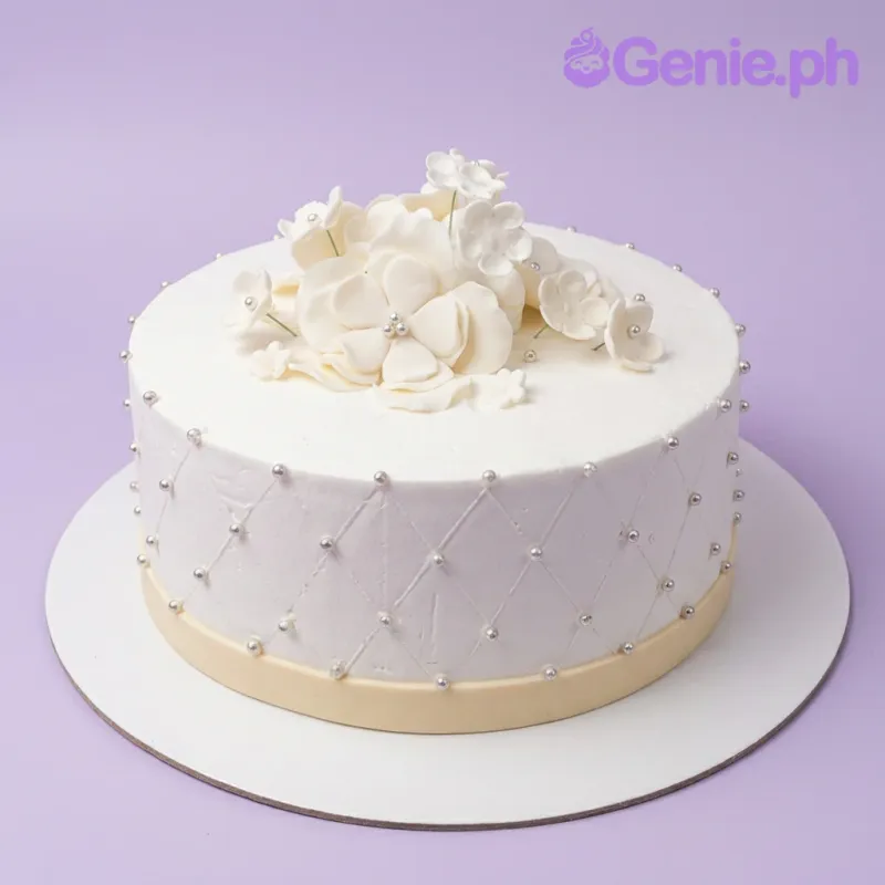 A white and silver 1-tier cake themed White Floral, featuring white gumpaste flowers, a quilted pattern, and silver dragees. A white and silver 1-tier cake themed White Floral, featuring white gumpaste flowers, a quilted pattern, and silver dragees.