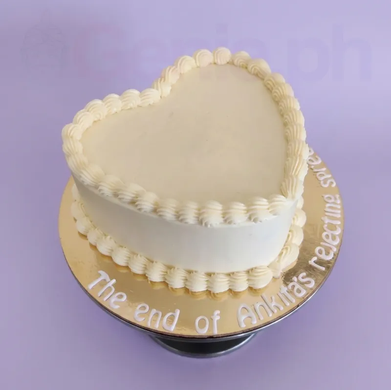 A white heart-shaped 1-tier cake, minimalist themed, with white piped shell borders, a personalized message, and a gold base board. A white heart-shaped 1-tier cake, minimalist themed, with white piped shell borders, a personalized message, and a gold base board.