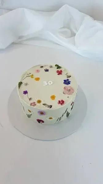 White 1-tier cake with smooth soft icing, wildflower theme, and edible pressed flower and greenery accents White 1-tier cake with smooth soft icing, wildflower theme, and edible pressed flower and greenery accents