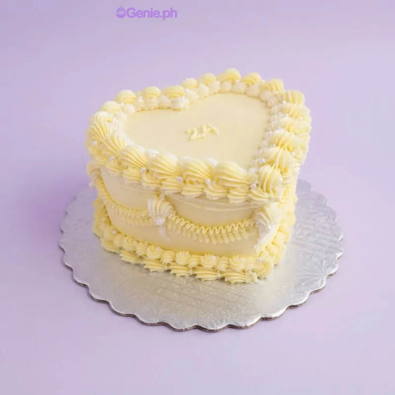 Light yellow heart-shaped cake with soft icing, piped yellow borders, white icing dots, and the number 24 on top Light yellow heart-shaped cake with soft icing, piped yellow borders, white icing dots, and the number 24 on top