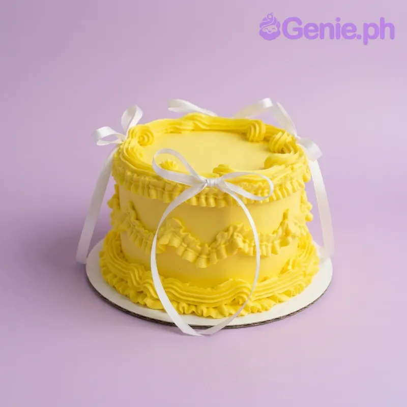 A yellow and white 1-tier cake themed around Yellow Vintage, featuring white ribbon bows and ruffled icing borders.