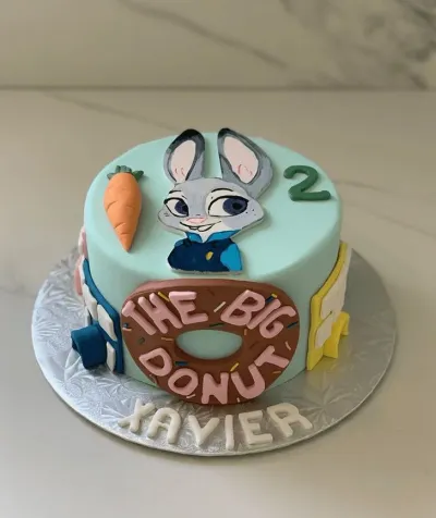 A light blue 1 Tier Fondant cake themed around Zootopia, featuring Judy Hopps, a large donut, a carrot, and personalized with Xavier. A light blue 1 Tier Fondant cake themed around Zootopia, featuring Judy Hopps, a large donut, a carrot, and personalized with Xavier.