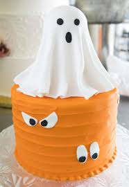 A photo of a Ghost themed cake. It is a blue 1 Tier cake decorated with a white ghost topper and ghost eyes.