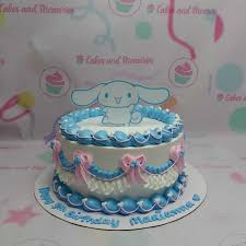 A photo of a Cinnamoroll themed cake. It is a white 1 tier cake decorated with a Cinnamoroll character printout, brown piped borders, brown garland-like decorations with pink bows, and 'Happy 1st Birthday Madianna' written in light blue.