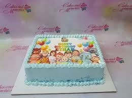 A photo of a Cocomelon themed cake. It is a Light Blue Rectangle cake decorated with a Cocomelon character printout and blue sprinkles.