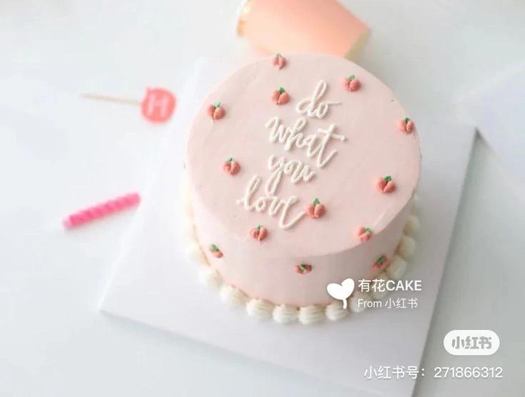 Pink minimalist cake with small peach icing decorations and white piped message 'do what you love'