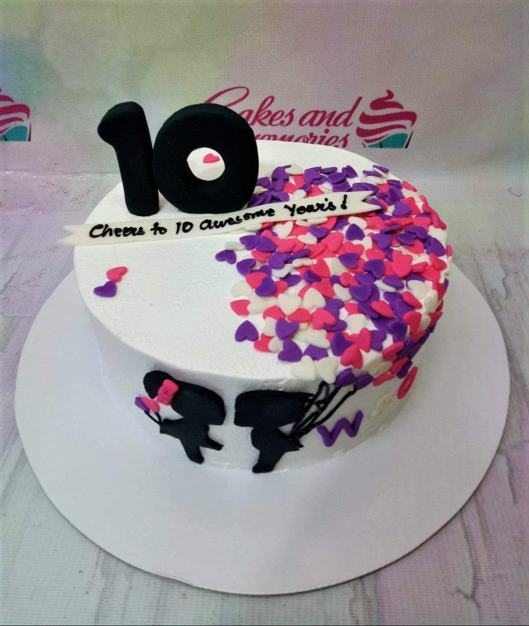 White minimalist cake with black number 10 topper, heart-shaped sprinkles, and silhouette figures of a couple.