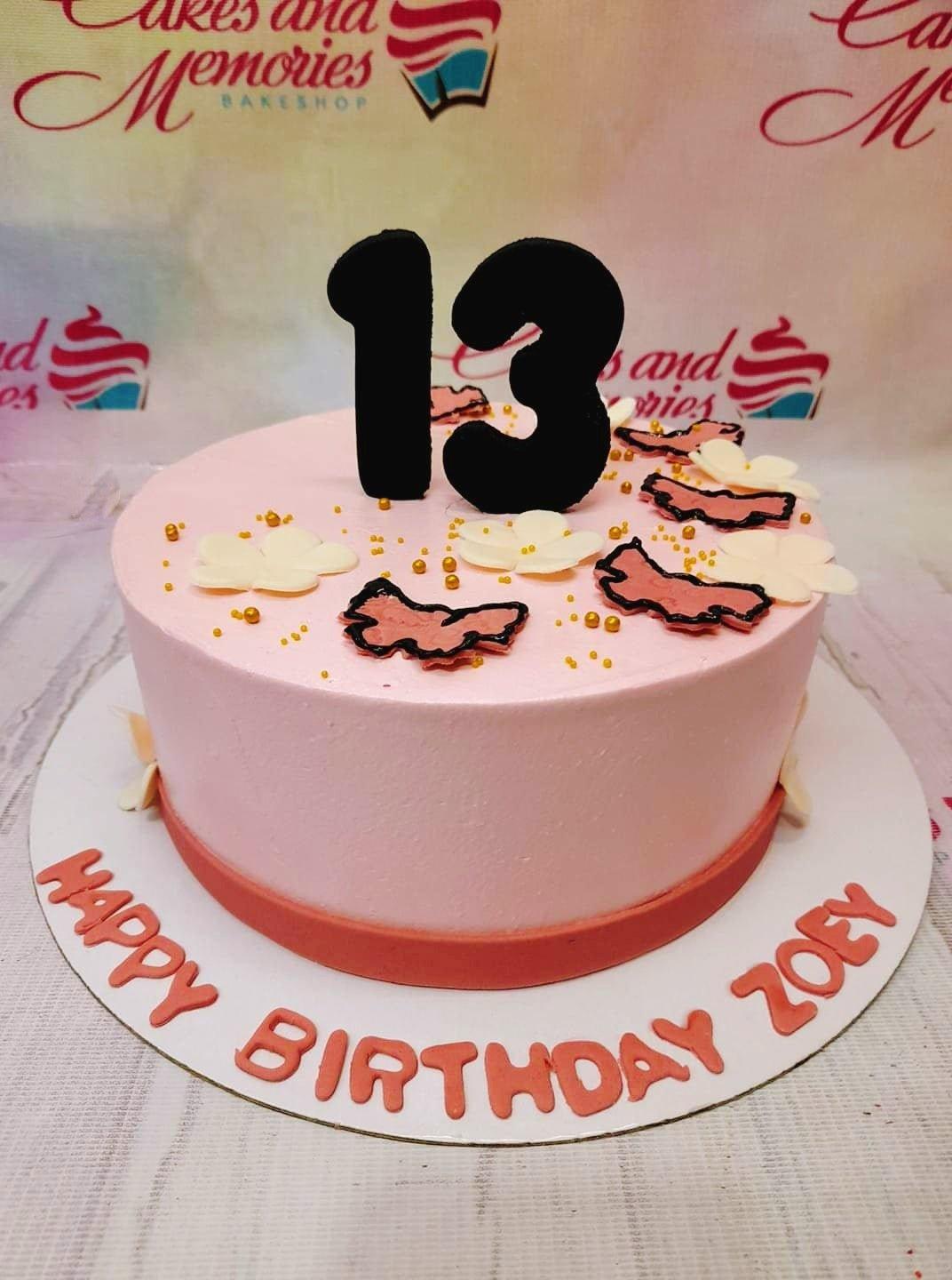 Pink minimalist birthday cake with black number 13 topper, white flowers, and gold dragees.