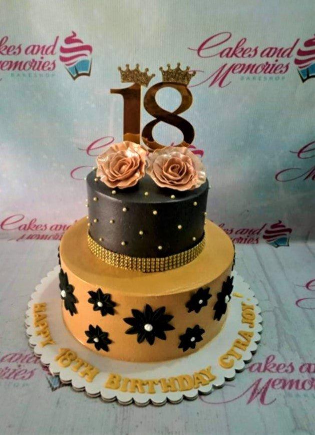 Elegant 2-tier black and gold 18th birthday cake with rose gold roses, gold beads, and a large number 18 topper.