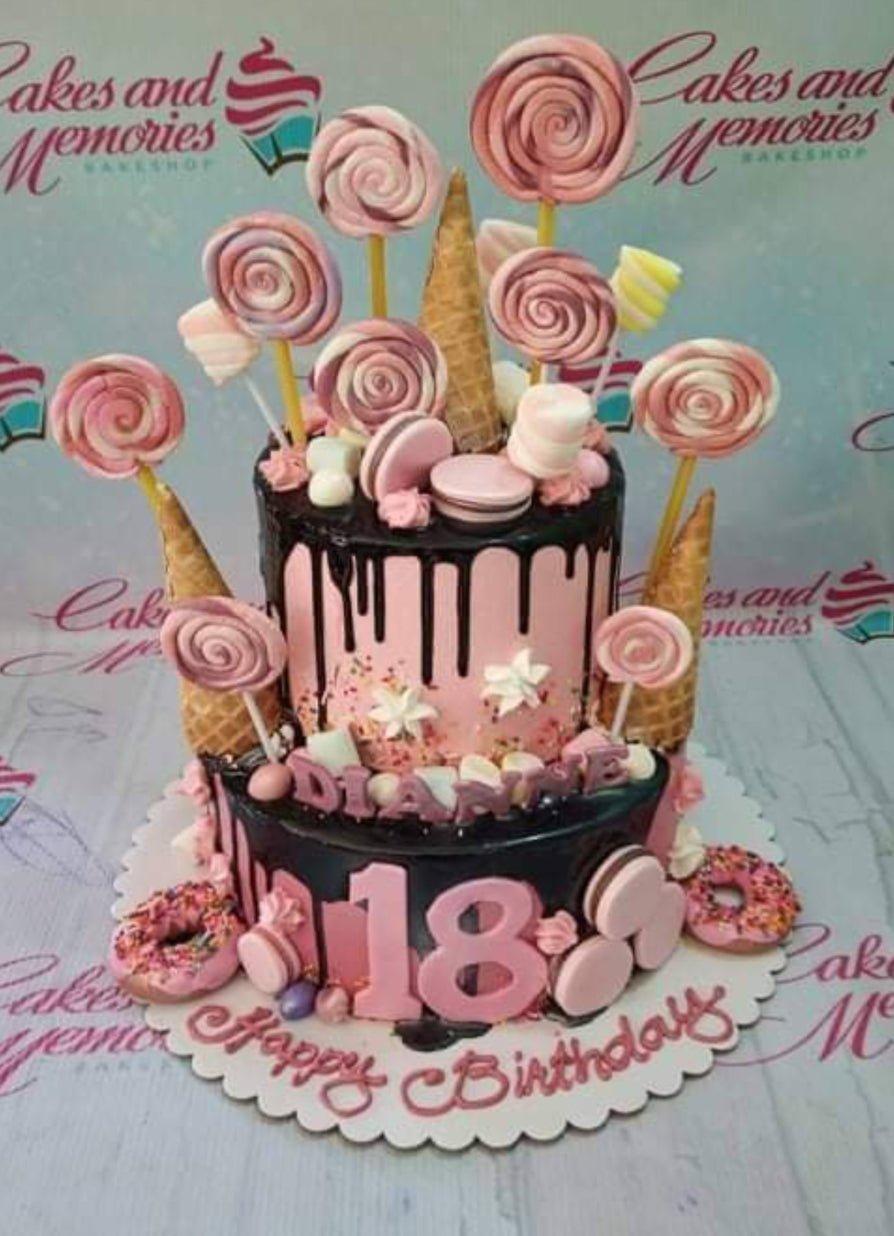 Pink and black 2-tier birthday cake with chocolate drip, lollipops, donuts, and macarons for an 18th birthday celebration.