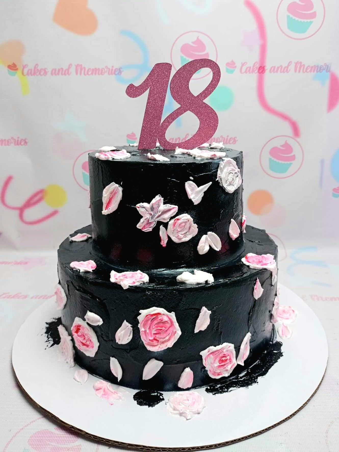 Two-tier black cake with pink and white palette knife icing roses and a glittery pink number 18 topper.