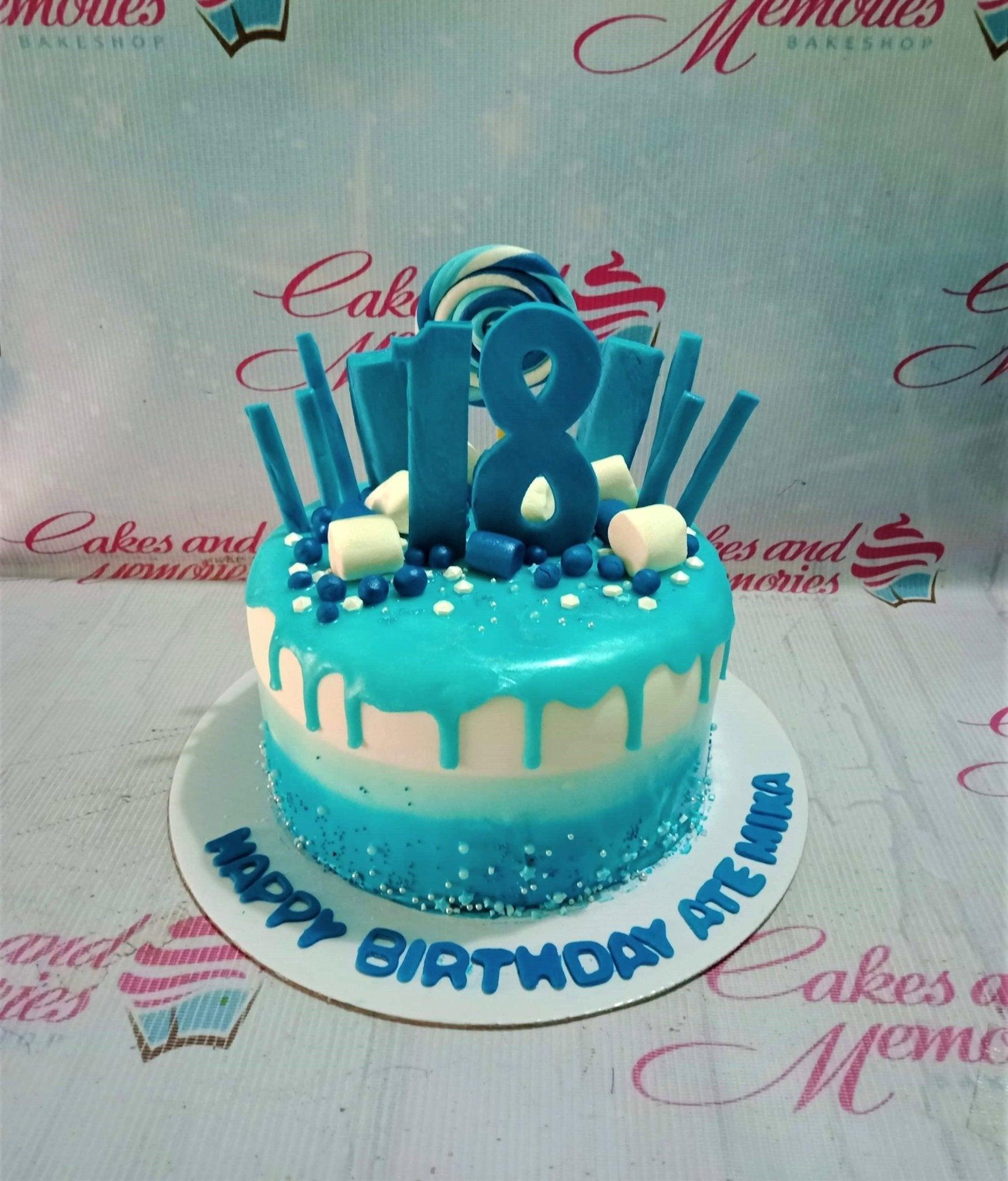 Blue and white ombre 18th birthday cake with a large blue number 18 topper, marshmallows, and blue lollipops.