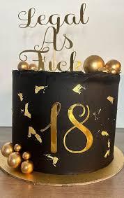 Black 18th birthday cake with gold leaf accents, gold spheres, and a 'Legal As Fuck' gold topper.