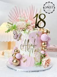 Elegant white textured cake with pink and gold spheres, artificial flowers, a butterfly, and a gold number 18 topper.
