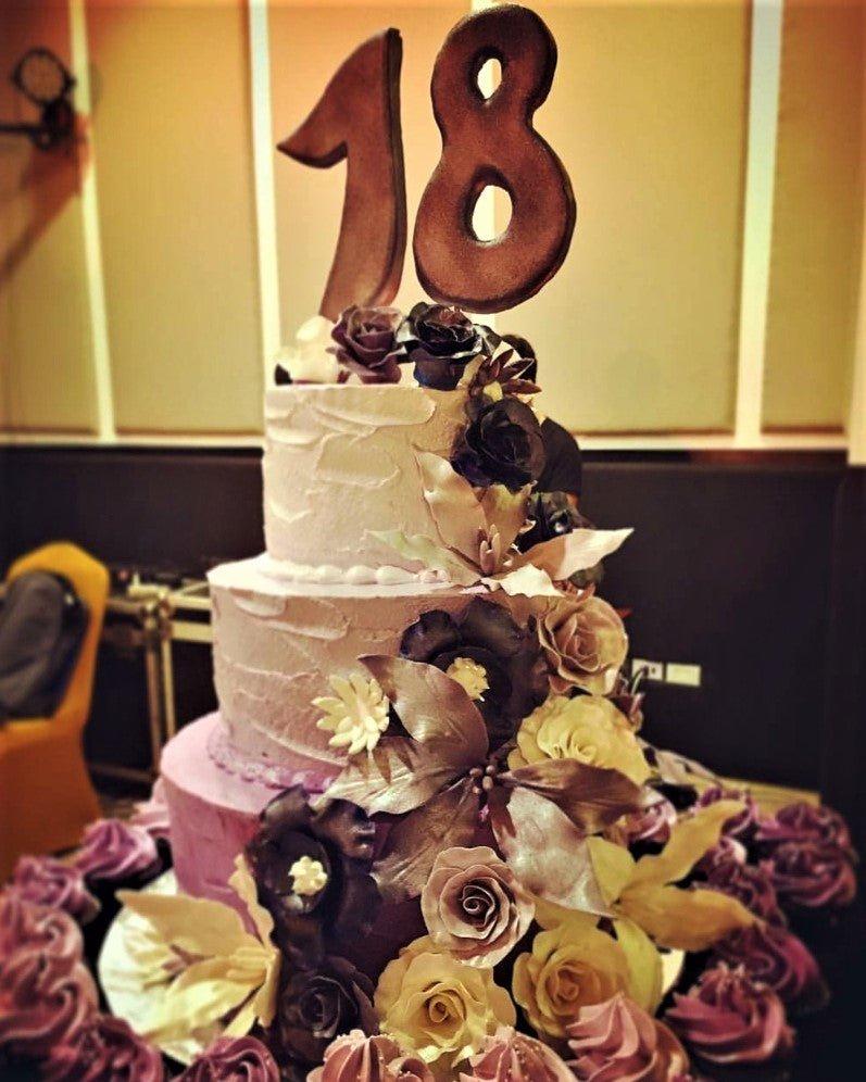 Elegant 3-tier purple and white floral cake with a large number 18 topper and dark purple roses.
