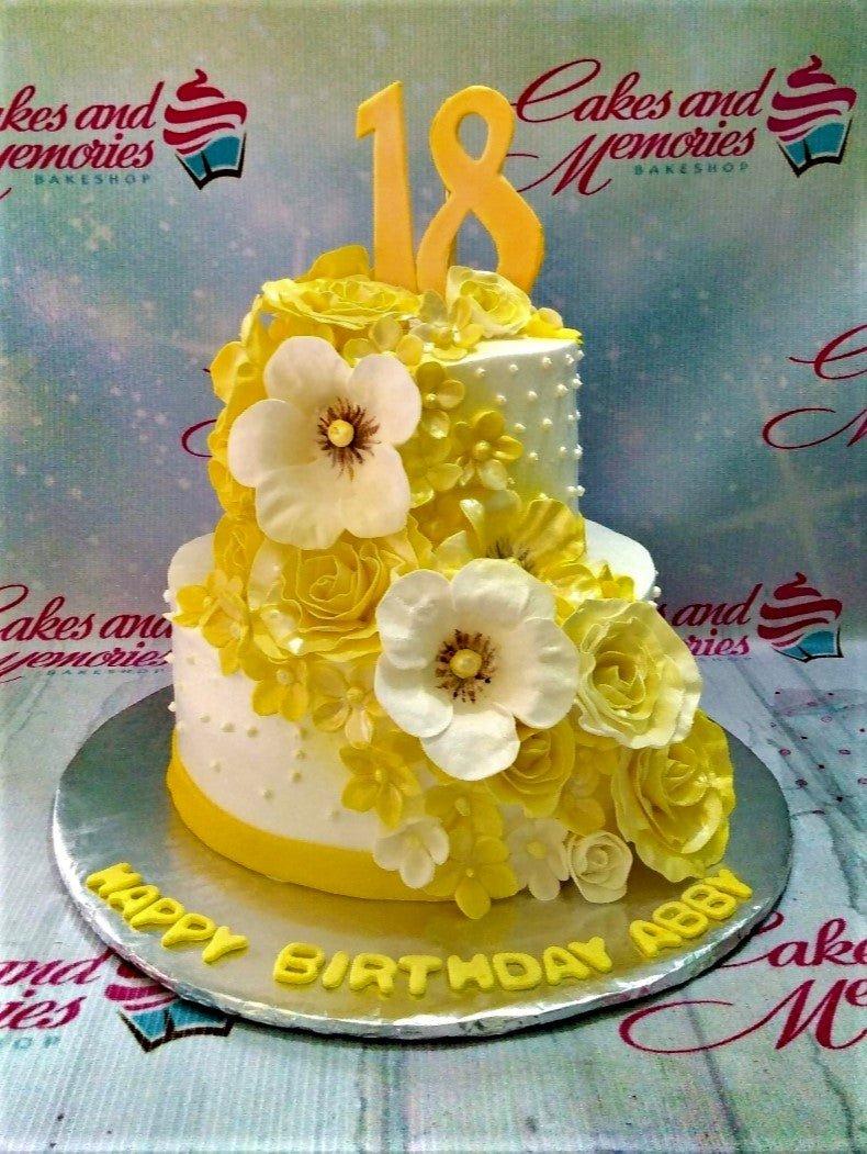 Yellow and white 2-tier floral birthday cake with large number 18 topper and gumpaste flowers.