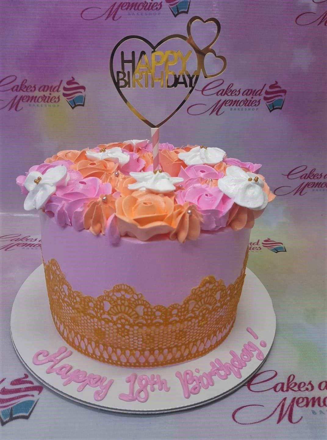 Pink 18th birthday cake with orange and pink icing rosettes, gold lace pattern, and a heart-shaped gold topper.