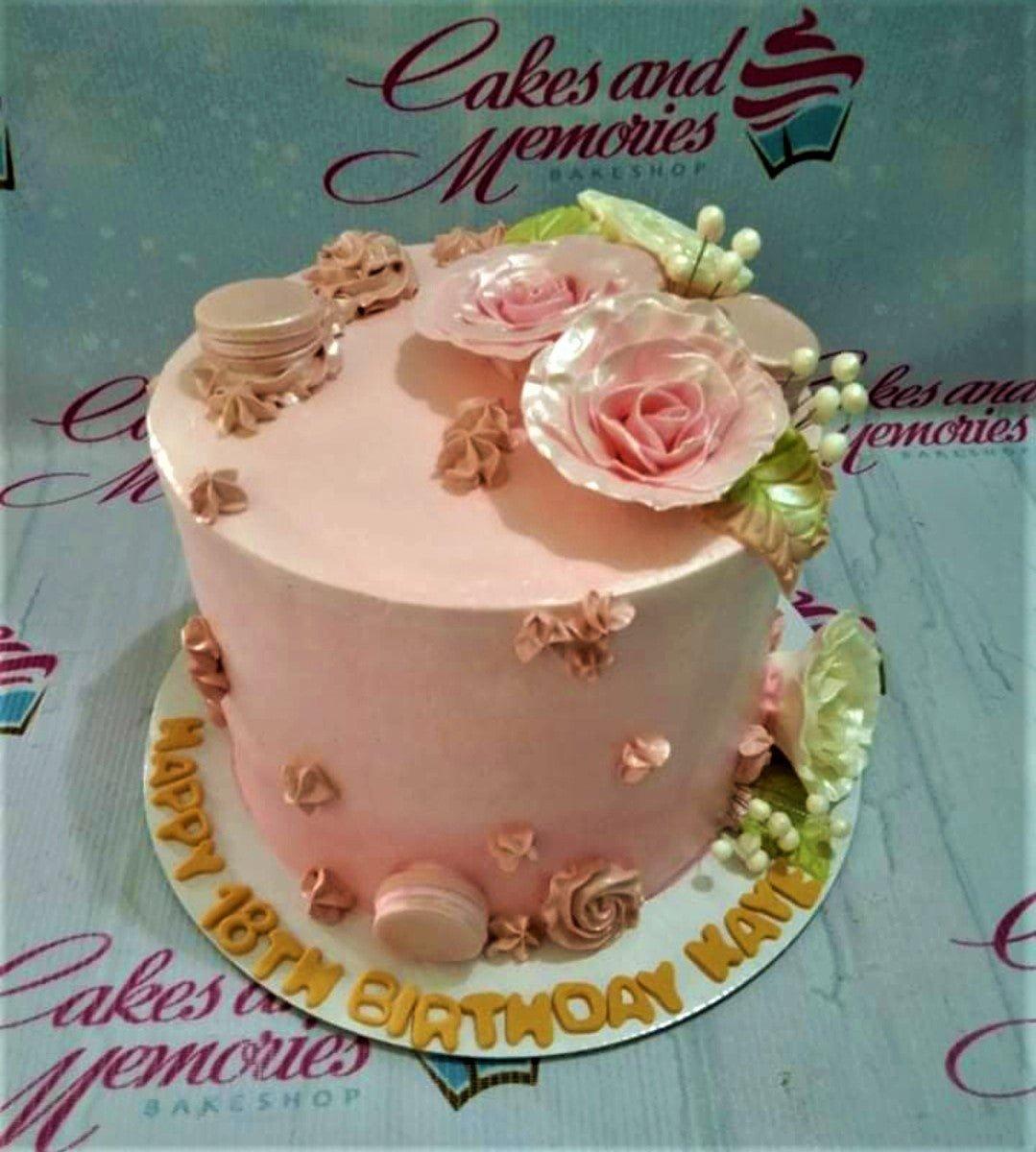 Pink 18th birthday cake with edible pink roses, macarons, and gold gumpaste letters on the base board.
