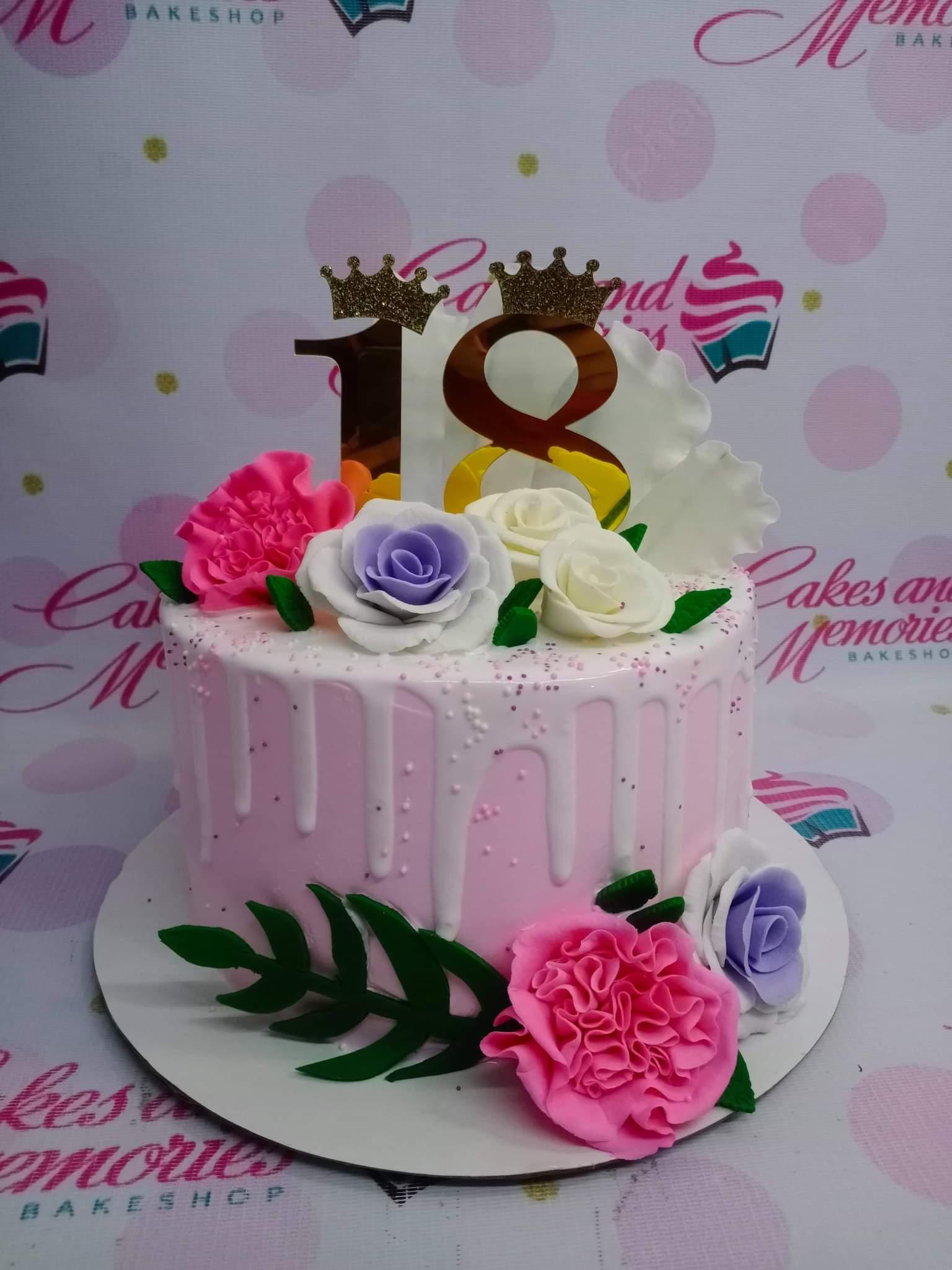 Pink 18th birthday cake with white drip, edible roses, and a gold number 18 topper with crowns.