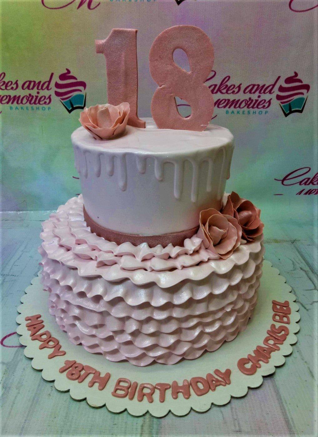 Two-tier pink birthday cake with ruffled icing on the bottom tier, smooth icing with drips on top, and gumpaste roses and number 18 topper.