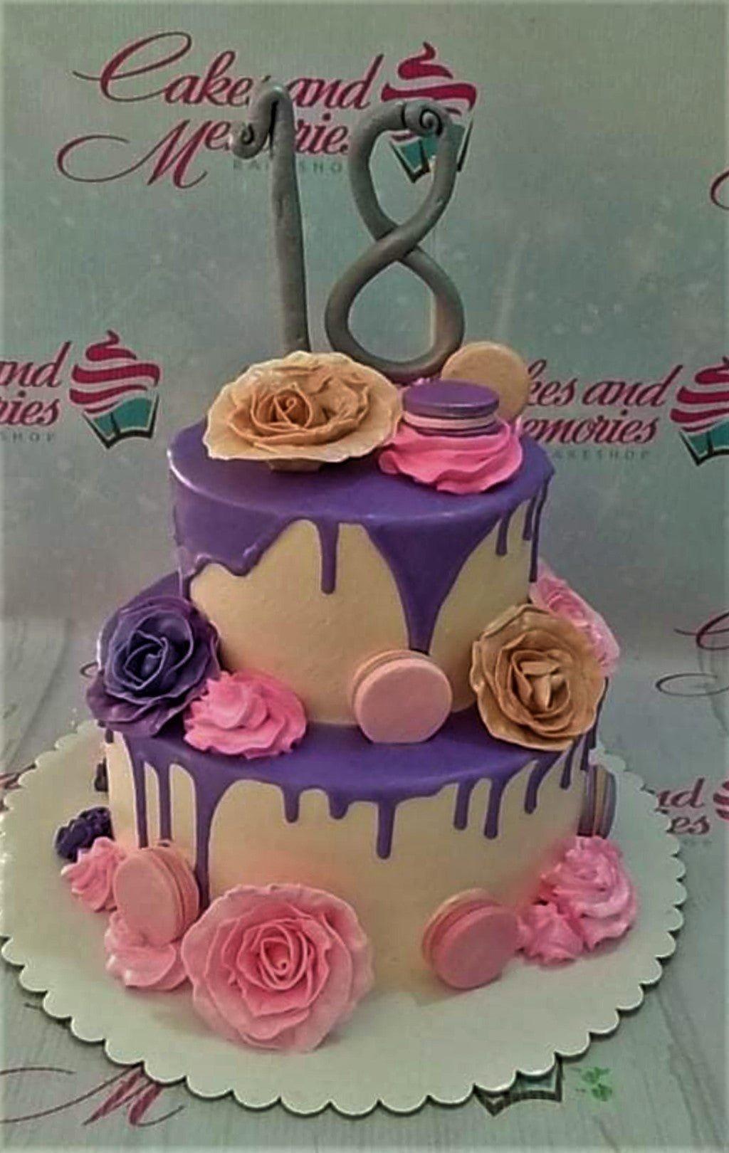 Two-tier beige cake with purple icing drips, pink and purple fondant roses, and a silver number 18 topper.
