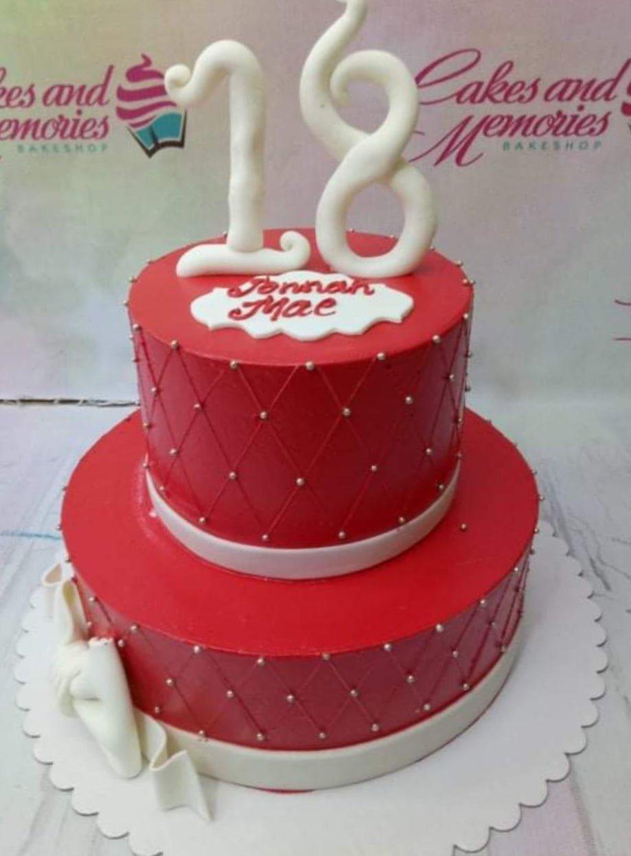 Red 2-tier 18th birthday cake with quilted pattern, silver dragees, white fondant bows, and a large white number 18 topper.