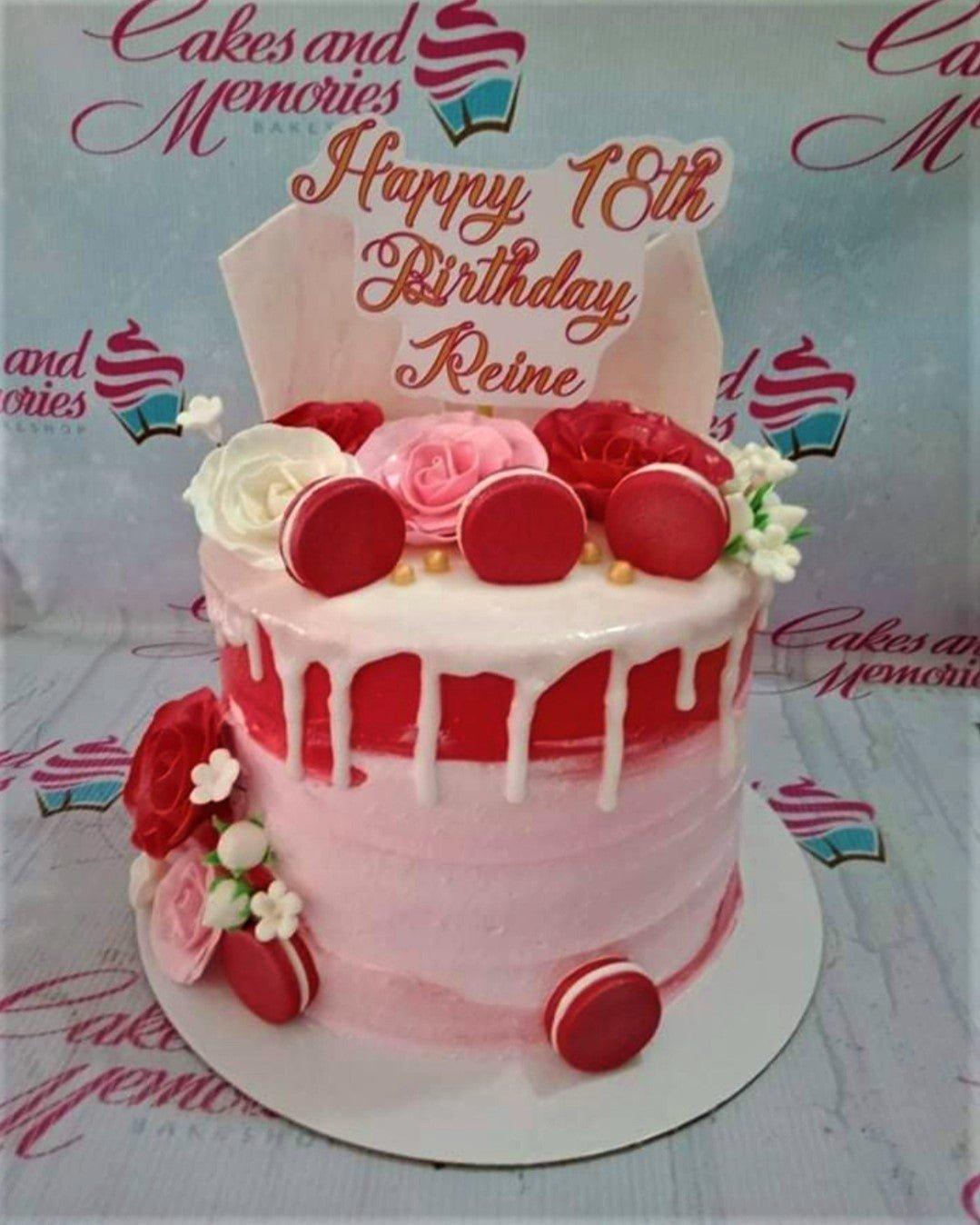 Pink and red ombre cake with white drip, red macarons, and pink and red roses for an 18th birthday.