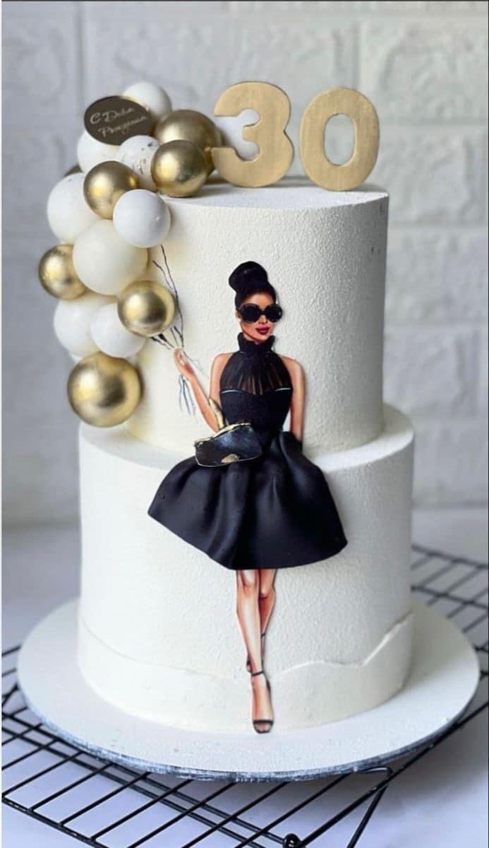 Elegant white 2-tier birthday cake featuring a stylish woman printout with a 3D fondant skirt and gold and white balloon decorations.