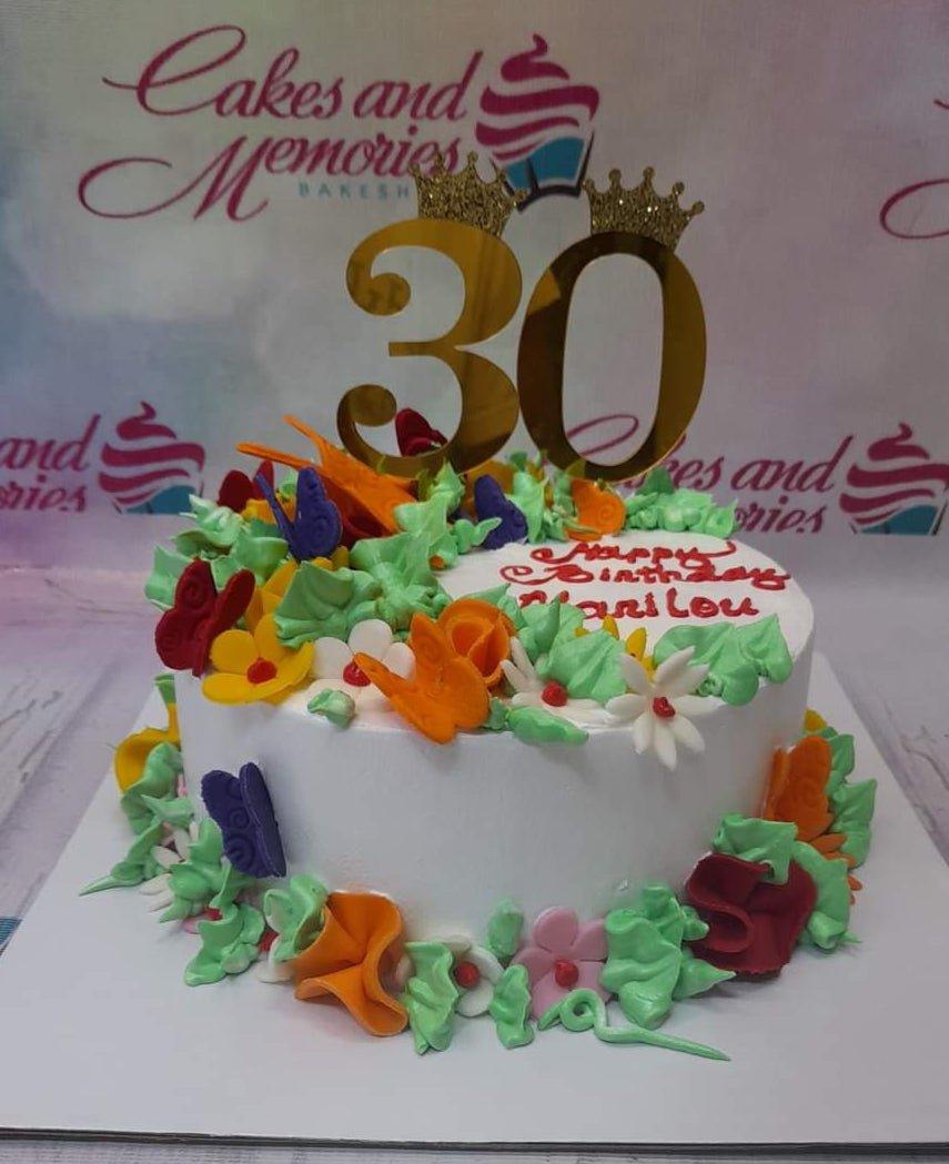 White round birthday cake with colorful gumpaste butterflies and flowers, featuring a gold 30 topper with crowns.