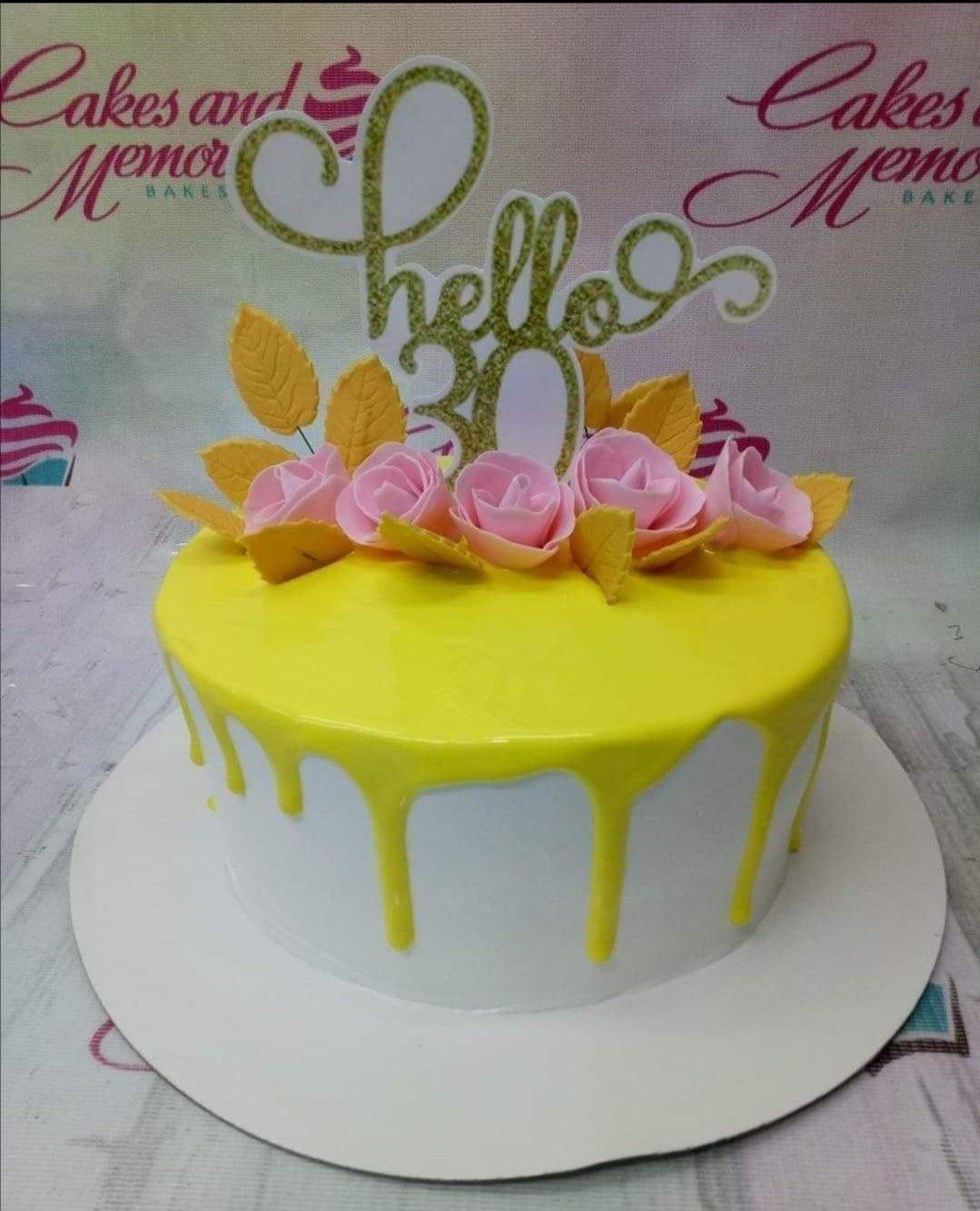 White 1-tier cake with yellow drip, pink fondant roses, yellow leaves, and a gold glitter Hello 30 topper.