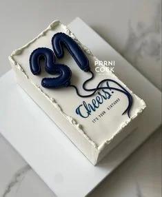A minimalist white rectangular cake with navy blue 3D balloon numbers 31 and a navy blue Cheers message.