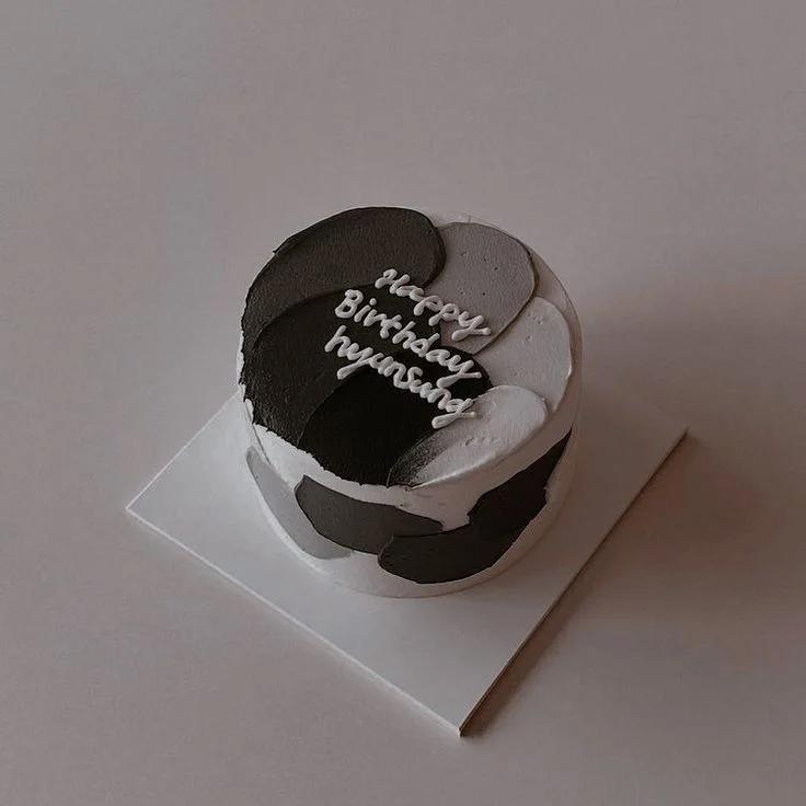 Minimalist white cake with black and grey palette knife icing strokes and white piped birthday message.