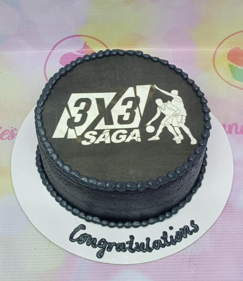Black minimalist cake with a 3x3 Saga basketball logo printout and a Congratulations message on the base board.