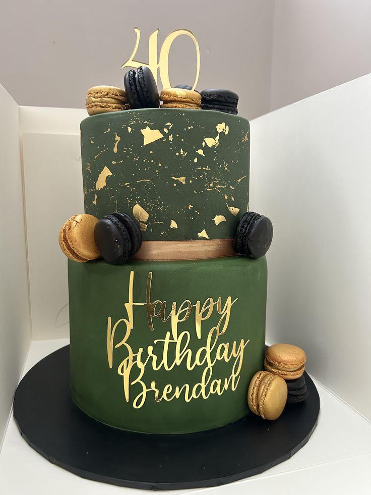 Two-tier dark green fondant cake with gold splatter, gold macarons, black macarons, and a gold 40th birthday topper.
