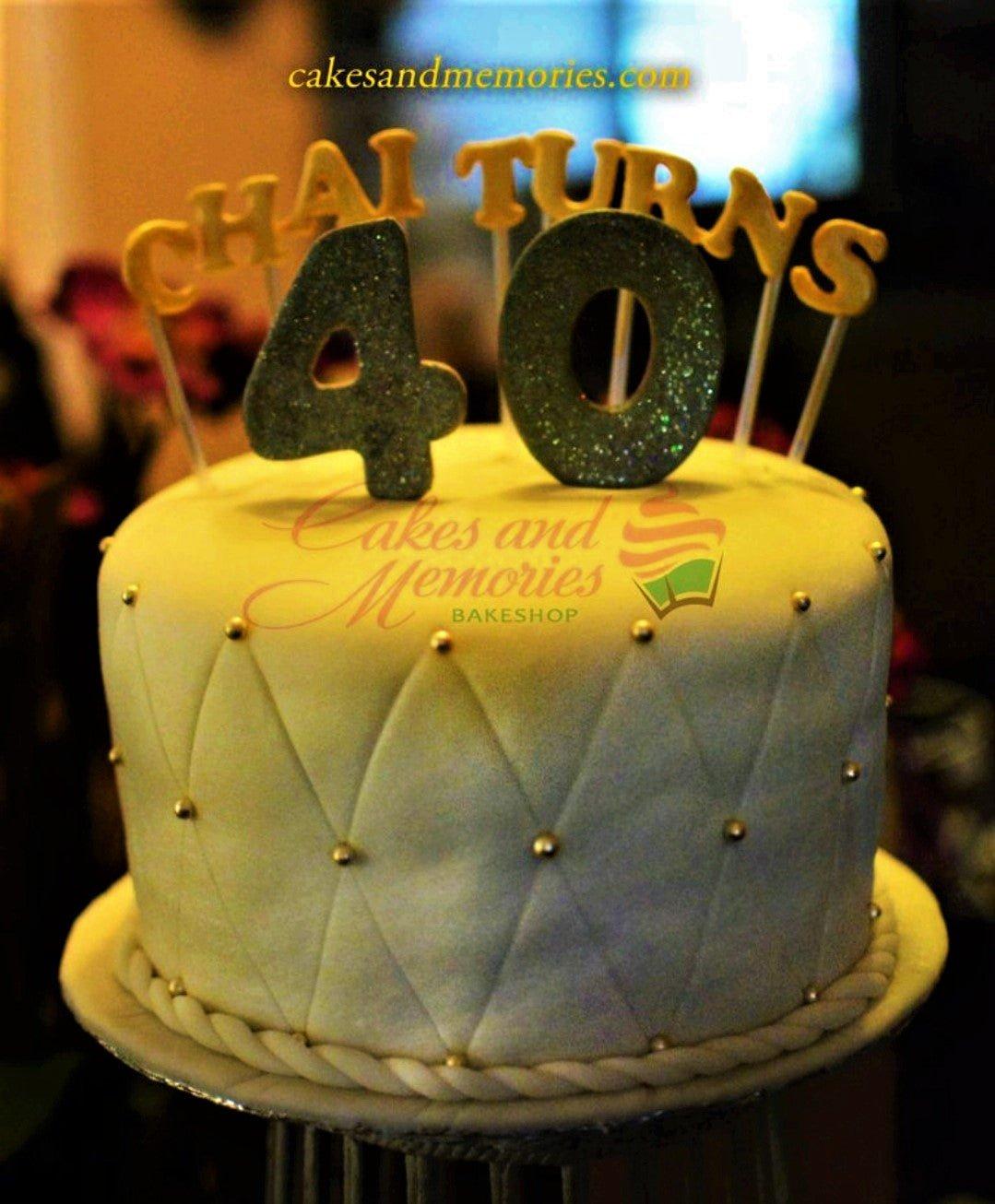 White fondant cake with quilted diamond pattern and gold pearls, topped with a glittery number 40 and Chai Turns message.
