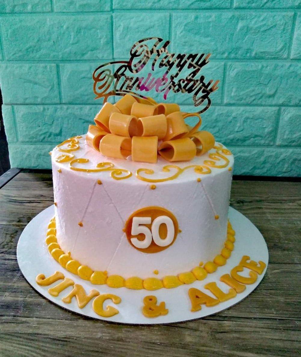 White 1-tier 50th anniversary cake with a large yellow fondant bow, gold topper, and yellow icing swirls.