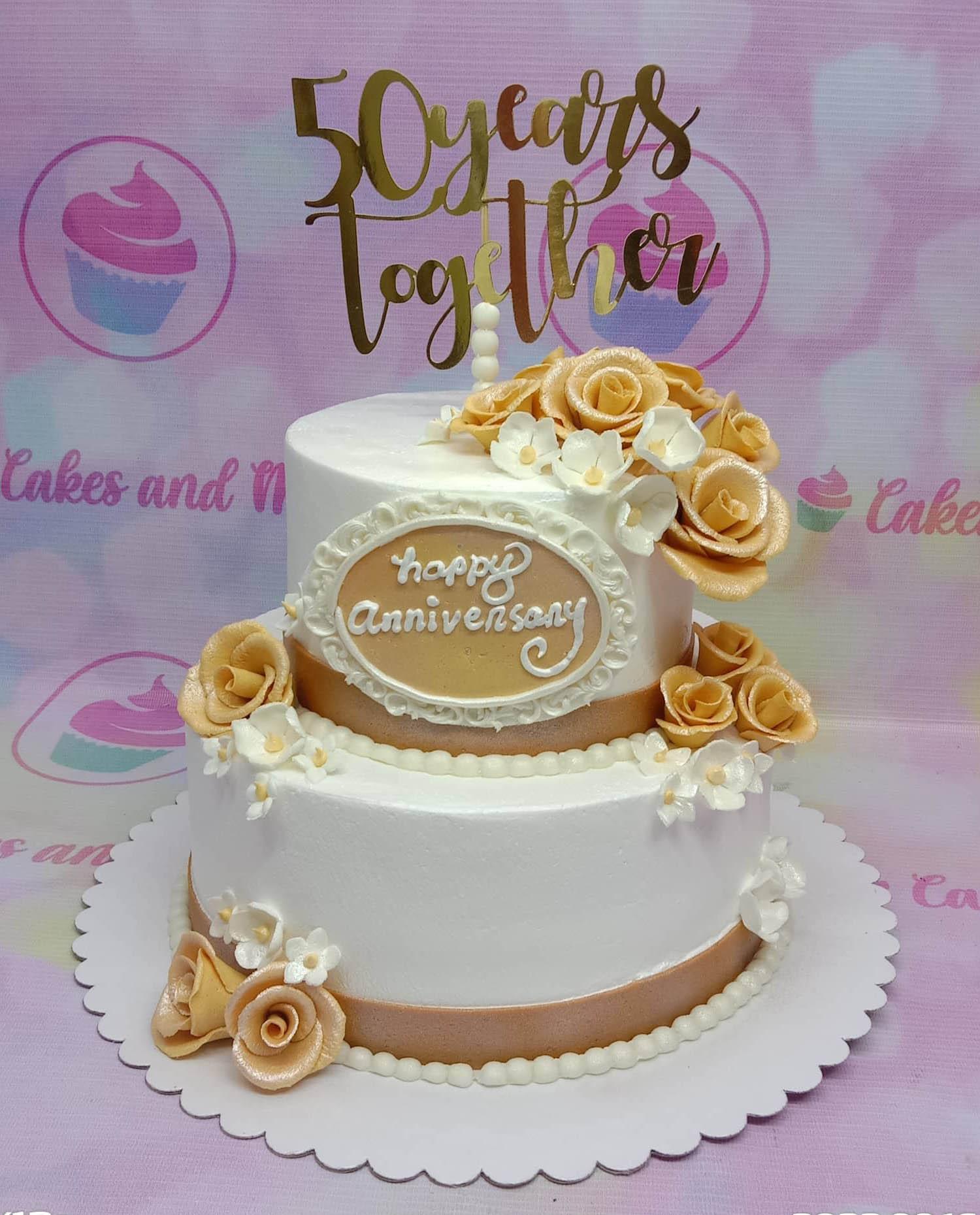 Elegant 2-tier white anniversary cake with gold roses, white blossoms, and a 50 years together gold topper.