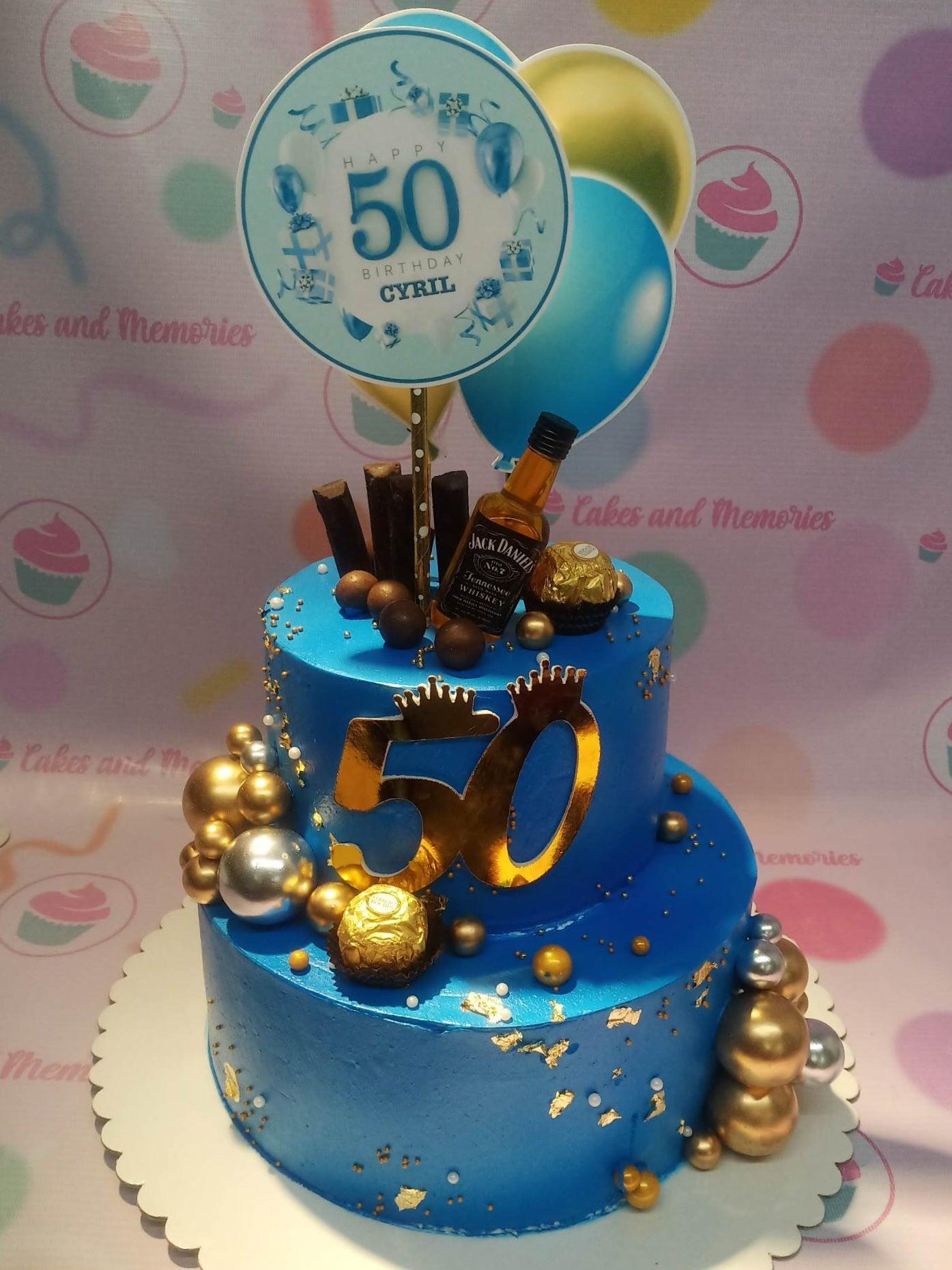 Blue 2-tier 50th birthday cake with Jack Daniels bottle, Ferrero Rocher chocolates, and gold balloon toppers.