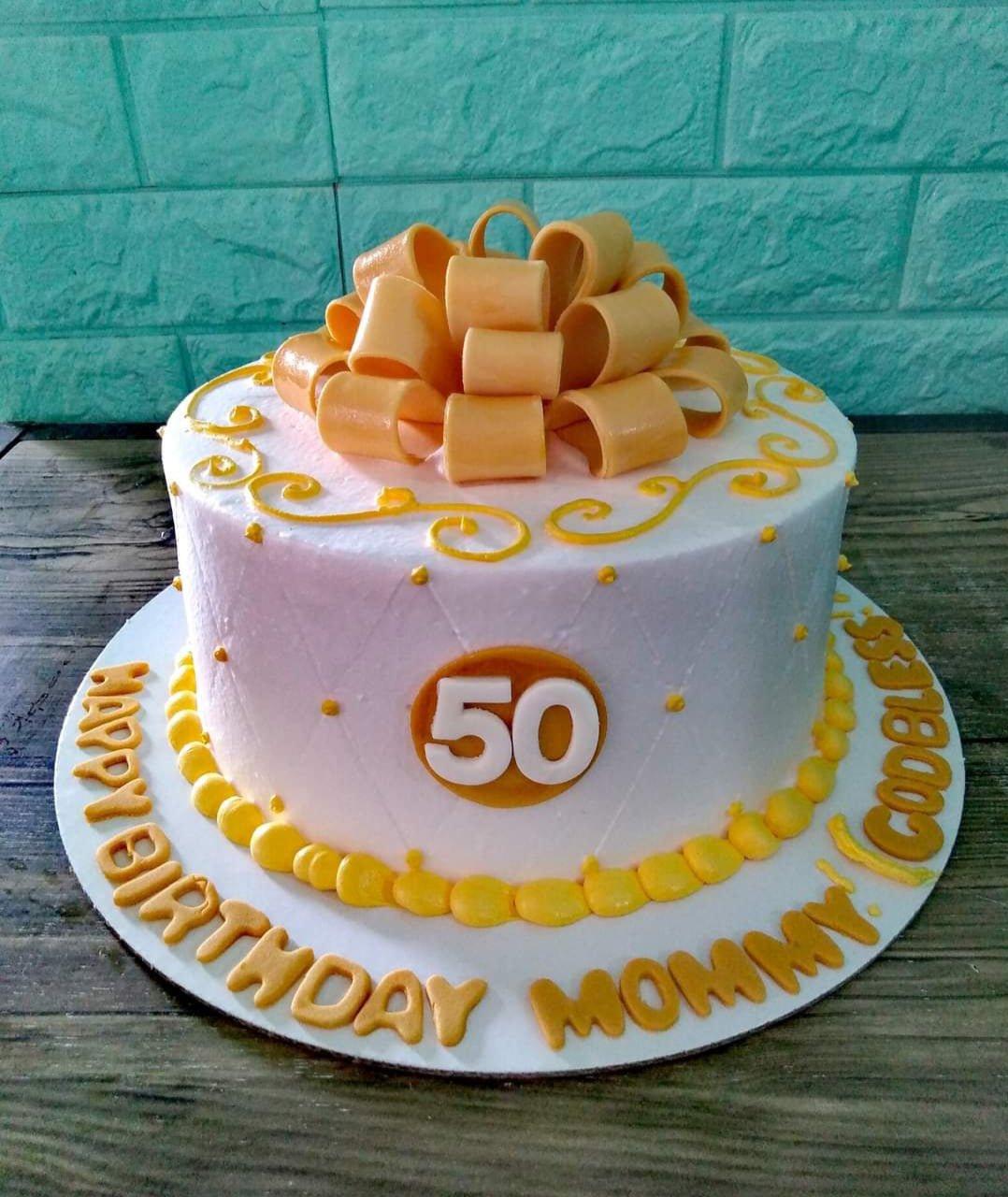 White 1-tier 50th birthday cake for Mommy with a large yellow fondant bow, quilted pattern, and yellow icing borders.