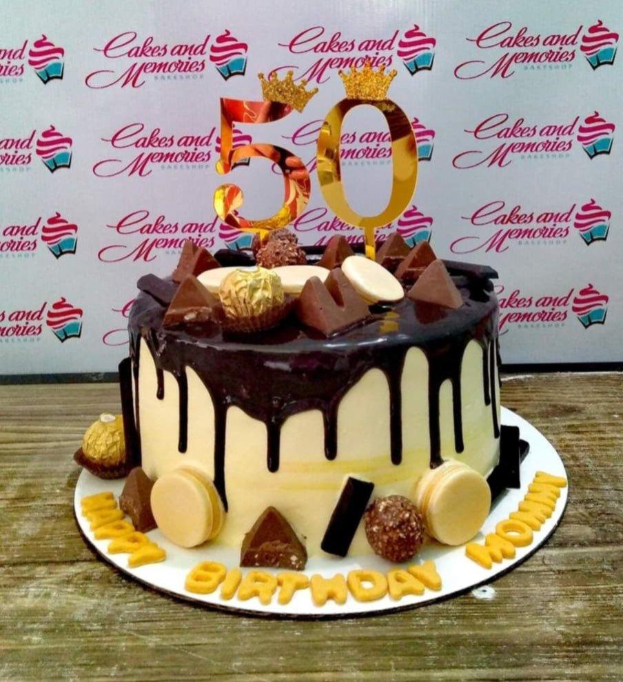Single tier white cake with chocolate drip, topped with Ferrero Rocher, chocolate triangles, and a gold 50 topper.