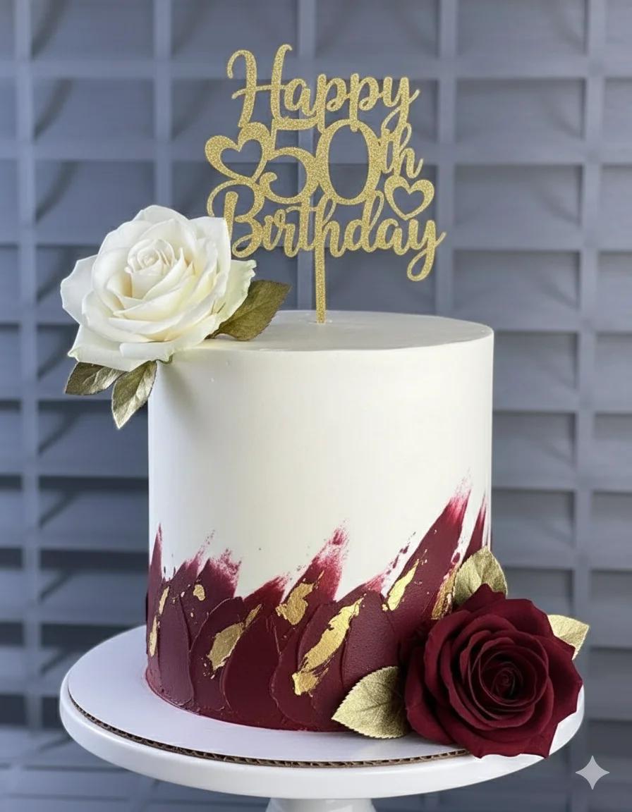 Elegant 1-tier 50th birthday cake with white icing, burgundy palette knife strokes, gold leaf accents, and large white and burgundy roses.